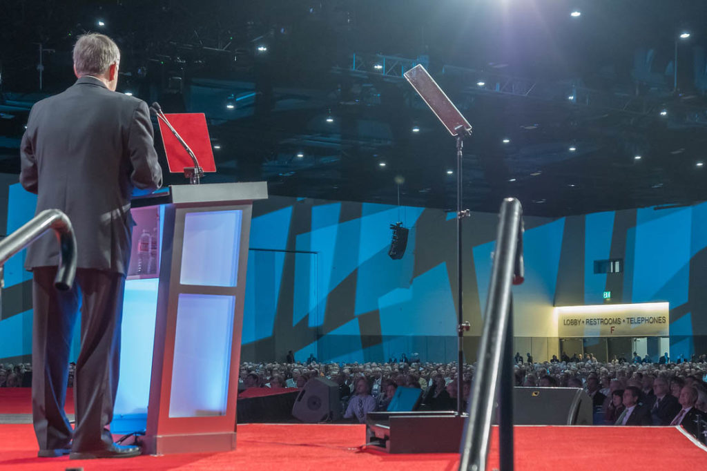 A view from behind the stage shows Lou Green of The Electric Cooperatives of South Carolina emceeing the first general session of the 75th NRECA Annual Meeting in San Diego. (Photo By: Luis Gomez Photos)