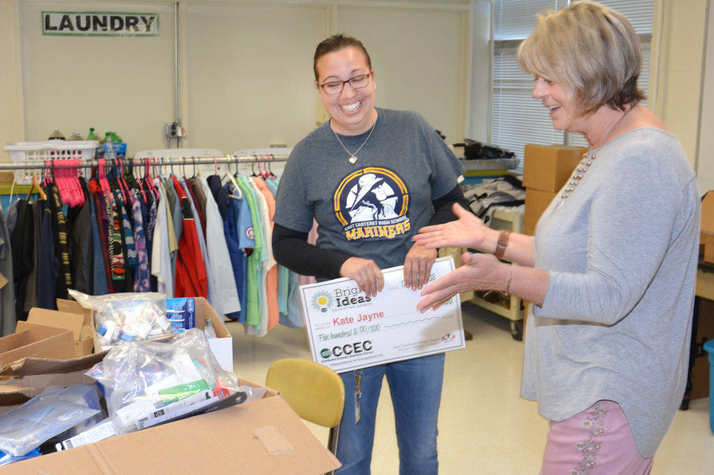 Sarah Grider of Carteret-Craven Electric Cooperative (right) was happy to give teacher Kate Jayne a check and toiletries from the co-op’s mutual aid supplies for the school’s food pantry. (Photo By: Lisa Taylor-Galizia/Carteret Craven EC)