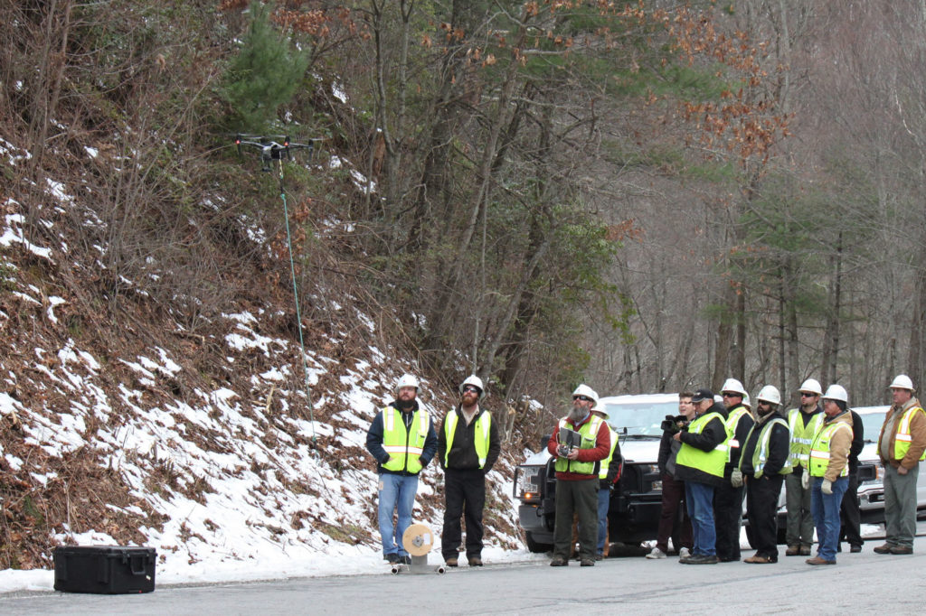 A Blue Ridge Mountain EMC crew watches a drone take off carrying a pull line to connect fiber to a weather station on an Appalachian Trail peak. (Photo By: Byron McCombs/ BRMEMC)