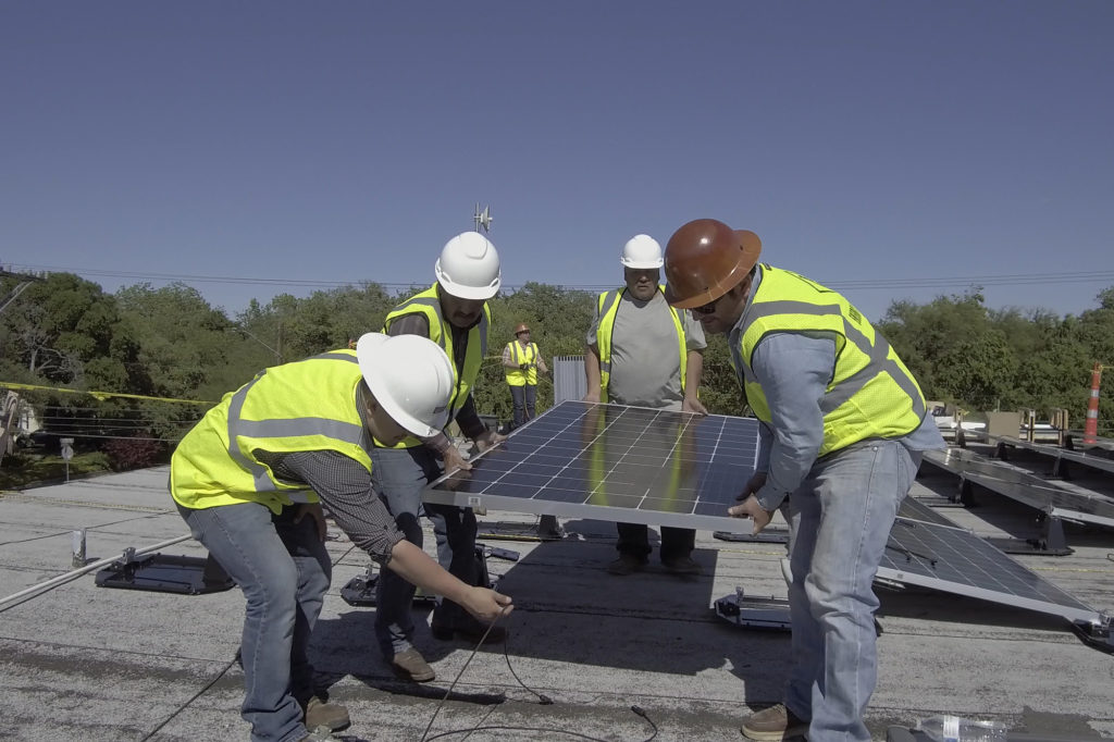 Installers lower a 75-pound solar panel into place on the roof of a business in San Antonio. The installation was BEC Solar’s first commercial solar project outside of its service territory. (Photo By: BEC)