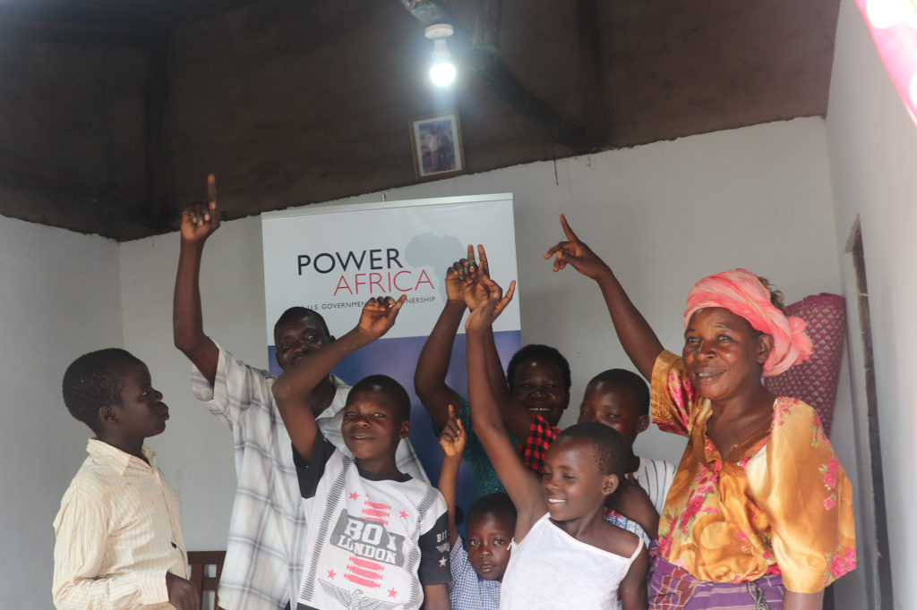 The family of Baraza Stephen and his wife, Annet Nyawere, celebrate after their home in Uganda was wired for electricity, allowing them to turn on the light for the first time. They are part of a pilot project using affordable home-wiring kits created by NRECA International at the request of USAID. (Photo By: Gail Birungi/Power Africa Uganda Electricity Supply Accelerator program, USAID)
