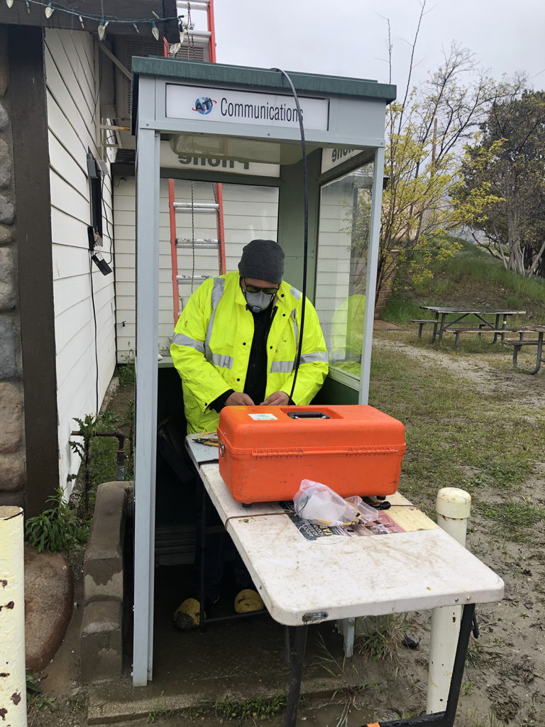 Donald Kay, a splicer for Anza Electric Cooperative in Southern California, works in an abandoned phone booth during a rainstorm. Anza serves an area of high poverty and unemployment that is suffering even more in the pandemic. (Photo courtesy of Anza Electric Cooperative)